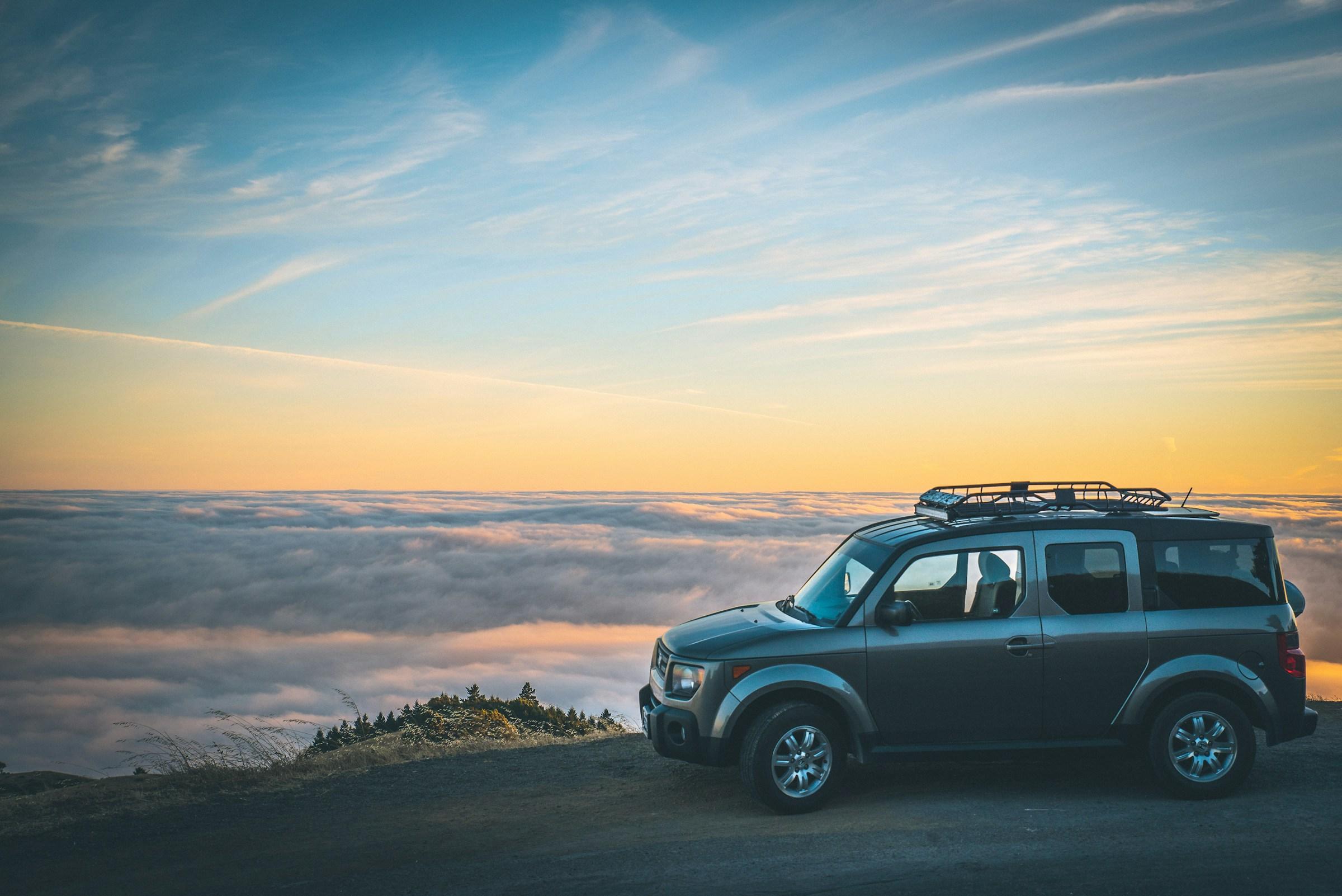 SUV mit Dachbox auf Bergstraße bei Sonnenuntergang